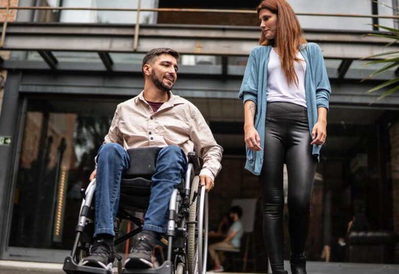 woman walking along side of man in wheelchair exiting building